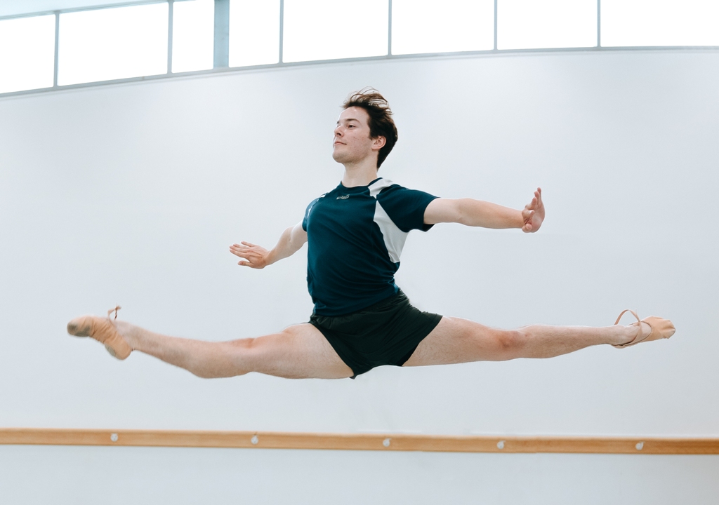 Male dancer in a studio performing a grand jete jump